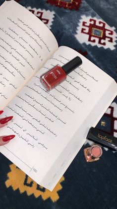 an open book with red nail polish and lipstick in it on a blue carpeted surface