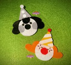 two felt animals wearing party hats on a green surface, one is black and the other is white