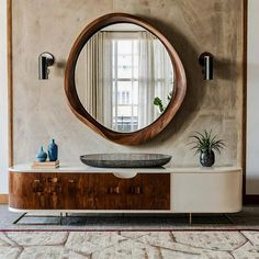 a round mirror hanging on the wall above a dresser with a bowl and plant in it