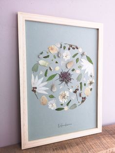 a white frame with flowers and leaves in it on a shelf next to a purple wall