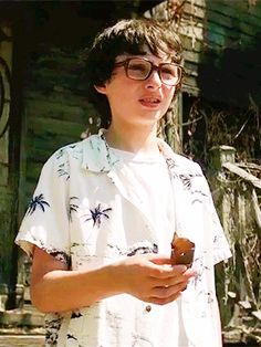 a young boy wearing glasses holding a donut in front of an old wooden building