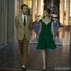 a woman in a green dress and a man in a beige suit walking down a hall