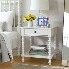 a bedroom with a white bed, nightstand and mirror on the wall next to it