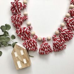 a red and white necklace with tassels next to a wooden house ornament