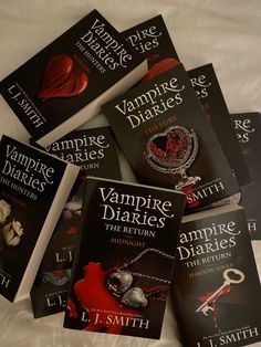 five vampire novels laying on top of a white bed with the covers pulled down and one has a red heart hanging from it