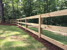 a wooden fence in the middle of a grassy area with trees and grass behind it