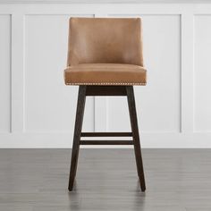 an upholstered bar stool with a tan leather seat and wooden legs in front of a white wall