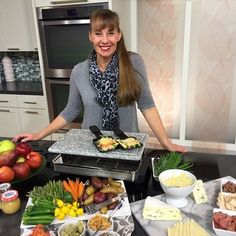 a woman standing in front of a table full of food and cheeses on it