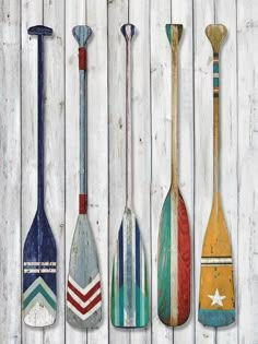 four paddles are lined up against a white wood wall, painted in different colors