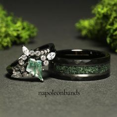 two wedding bands with green stones and crystals on them, sitting next to each other