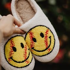 someone is holding up some slippers with smiley faces on them and one has a baseball ball in it