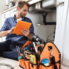 a man sitting on the floor with tools in his hands and looking at an orange folder