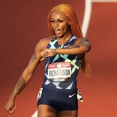 a woman with red hair and tattoos on her arm pointing to the side while standing in front of a track