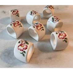 six white cups with flowers painted on them sitting on a counter top next to each other