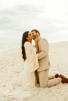 a man and woman sitting on the beach kissing