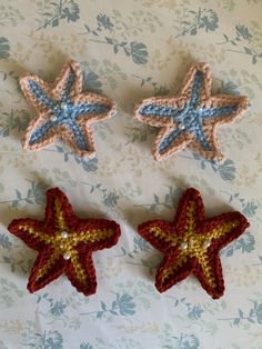 three crocheted stars are laying on a floral surface, one is red and the other is blue