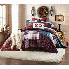 a bed with plaid comforter and pillows in a room next to a christmas wreath