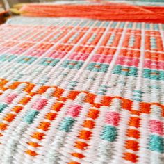 an orange, white and blue crocheted blanket on a bed