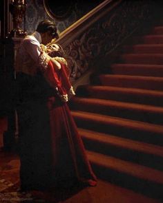 a man and woman embracing on the steps of a staircase in an old fashion dress