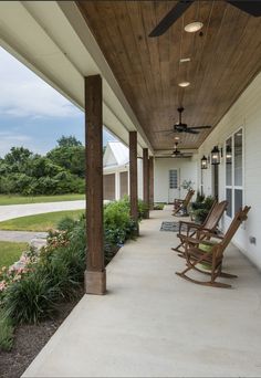 two rocking chairs on the front porch of a white house with wood trim and ceiling fans