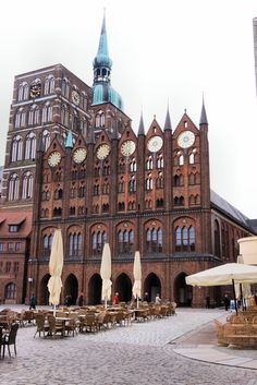 an old building with tables and umbrellas in front of it on a cobblestone street