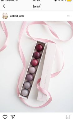 an open box with chocolates in it on a white table next to a pink ribbon