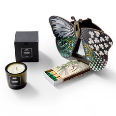 This image features a whimsical and artistic gift collection. The centerpiece is a butterfly-shaped decorative item with intricate patterns and vibrant colors. Accompanying this is a box of matches with a nature-themed design and a Petitgrain scented candle by Casa Posta, housed in a simple, elegant glass jar. The combination of the butterfly, matches, and candle creates a playful yet sophisticated ensemble, perfect for someone who appreciates unique and creative decor elements. Gardening Gift Box, Hidden Mirror, Dragonfly Illustration, Game Night Gift, Luxury Gift Boxes, Small Butterfly, Butterfly Decor, Butterfly Wall Decor, Vibrant Patterns