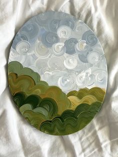 a round plate with green, yellow and white swirls painted on the surface in front of a white sheet