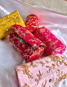 four different colored bags sitting on top of a white cloth covered tablecloth with gold and red designs