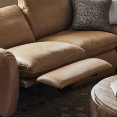 a brown leather couch sitting on top of a wooden table next to a white vase