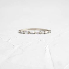 a thin white gold band with five baguettes set in the middle on a plain surface