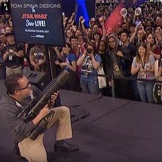 a man sitting on top of a stage holding a giant object in front of a crowd