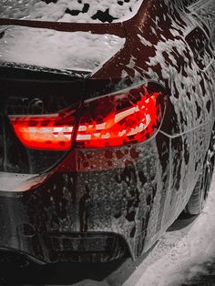 the back end of a car covered in snow and ice with red tail lights on