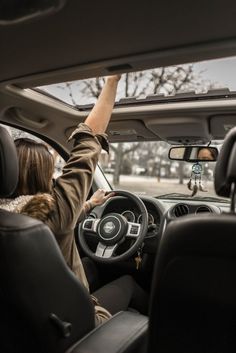 a woman driving a car with her hand up in the air and steering wheel down