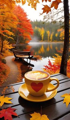 a cup of coffee sitting on top of a wooden table next to autumn leaves and a bench