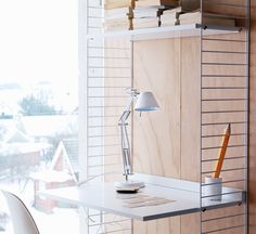 a desk with a lamp on it next to a wall mounted book shelf and chair