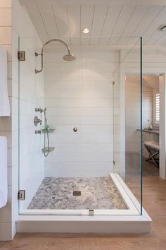 a walk in shower sitting next to a white towel on a rack and wooden floor