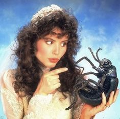 a woman in a white dress holding a black lizard and pointing to it's face