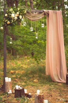 an outdoor ceremony with candles and flowers on the ground in front of a wooden arch