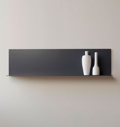 two white vases sitting on top of a black shelf next to a gray wall