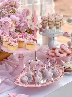 a table topped with pink cupcakes and other desserts covered in frosting