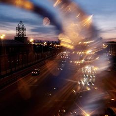 blurry photograph of city street at night with buildings and lights in the background, taken from an overpass