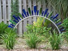 a circular sculpture made out of blue glass bottles in the grass next to a wooden fence