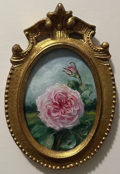 a painting of a pink rose in a gold frame on the wall next to a white wall