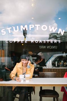 a woman sitting at a table in front of a coffee shop talking on her cell phone