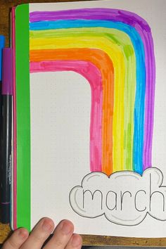 a hand holding a marker next to a drawing of a rainbow and the word march