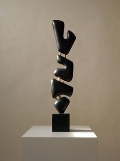 a black sculpture sitting on top of a white pedestal in front of a beige wall