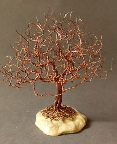 a wire sculpture of a man standing next to a tree on top of a rock