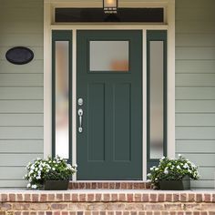 a green front door with two planters on the steps and a light above it