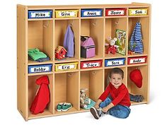 a young boy sitting on the floor in front of a wooden cubby with toys